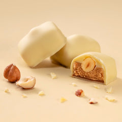 𝐌𝐚𝐧𝐨𝐧 𝐂𝐚𝐟𝐞́ 𝐰𝐡𝐢𝐭𝐞 -înveliș fin din ciocolată albă cu umplutură delicioasă: cremă de unt infuzată cu cafea Arabică 100%, așezată peste un strat subțire de cremă pralinată, acoperită cu o alună de pădure întreagă